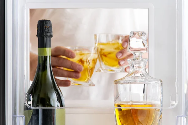 Open hatch of a mini bar in a modern refrigerator. home mini bar in the fridge. a man took two glasses with alcohol from the counter, view from the refrigerator. — Stock Photo, Image