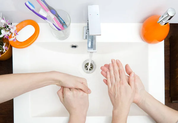 Δύο άνθρωποι πλένουν τα χέρια τους με σαπούνι κάτω από τρεχούμενο νερό σε λευκό νεροχύτη. Από κοντά. προστασία από ιούς πλύνετε τα χέρια σας. — Φωτογραφία Αρχείου