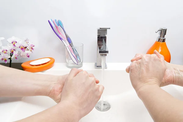 Δύο άνθρωποι πλένουν τα χέρια τους με σαπούνι κάτω από τρεχούμενο νερό σε λευκό νεροχύτη. Από κοντά. προστασία από ιούς πλύνετε τα χέρια σας. — Φωτογραφία Αρχείου