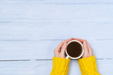 Fotokopi alanı olan eski ahşap masa manzaralı kahve fincanı. Sıcak, sarı ev kazağı giymiş bir kadın elinde bir kupa kahveyle içkinin tadını çıkarıyor..