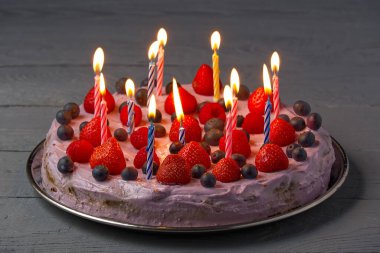 Böğürtlenli ve doğum günü mumlu ev yapımı peynirli kek. Çilekli cheesecake, yaban mersini ve ahududu ile gri ahşap arka planda