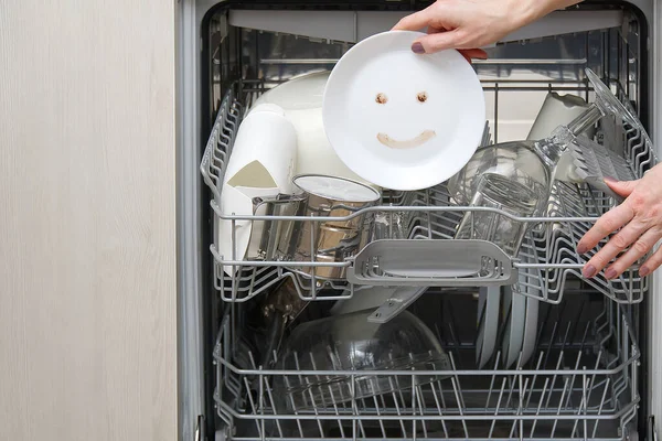 Fine washed dishes in the dishwasher. Integrated Dishwasher with white plates front vew and happy emotion on plate. Easy home cleaning concept.