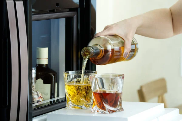 Offene Luke einer Minibar in einem modernen Kühlschrank. Minibar zu Hause im Kühlschrank. der Besitzer schenkt den Gästen alkoholische Getränke, Whiskey, Cognac in Gläser ein — Stockfoto