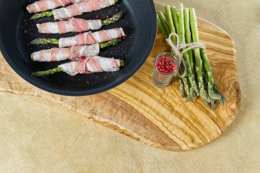 Kızartma tavasında kuşkonmaz etrafında lezzetli pastırma. Tahtada pişmeye hazır taze kuşkonmaz. Sağlıklı yemek tarifleri kavramı.