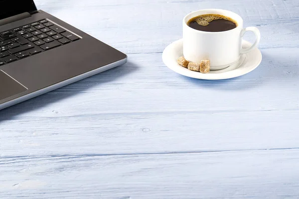 Laptop egy csésze kávét világoskék régi fa asztal. Jegyzetfüzet egy csésze friss kávéval az irodában. Otthonról történő munkavégzés — Stock Fotó