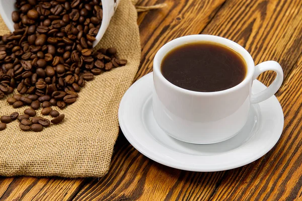 Taza de café blanco con bebida aromática de café en la mesa de madera marrón. Semillas de café en mesa de madera antigua con taza de bebida de café — Foto de Stock