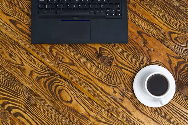 Laptop egy csésze kávéval a régi barna fa asztalon. Felülnézet Notebook csésze friss kávé otthoni irodában a faluban. — Stock Fotó