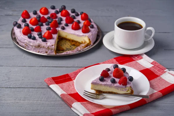 Stück hausgemachter Käsekuchen mit Beeren auf Teller und Tasse Americano-Kaffee. Käsekuchen mit Erdbeere, Blaubeere und Himbeere auf grauem Holzhintergrund. — Stockfoto