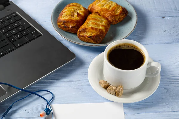 Laptop csésze kávé és pékség világoskék régi fa asztal. Jegyzetfüzet egy csésze friss kávéval az irodában. Otthonról történő munkavégzés — Stock Fotó