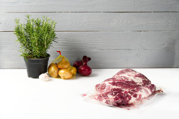 raw pork meat in vacuum with Fresh Onion, garlic and rosemary. Healthy Cooking industry concept at home