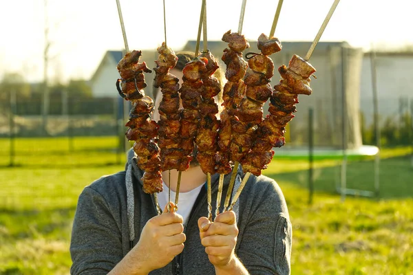 Mão com polegar para cima segurando espetos com shashlik. homem detém espetos com kebab preparado. Churrasco — Fotografia de Stock