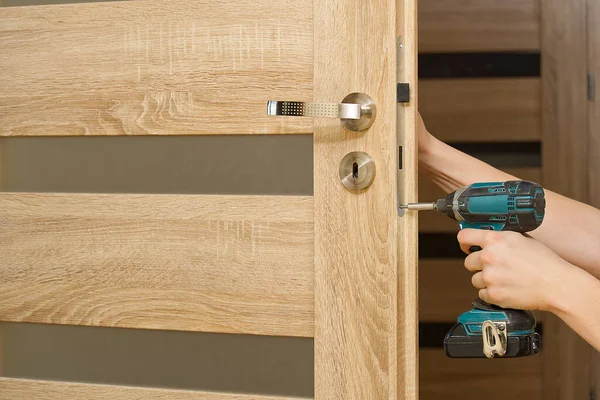 handyman repair the door lock in the room. man repairing the door handle furniture. carpenter at lock installation with electric drill into interior wood door