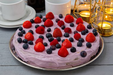 Ev yapımı çilekli cheesecake. Çilekli cheesecake, böğürtlen ve ahududu gri ahşap masa üzerinde mumlar ve tabaklar ile süslenmiş.