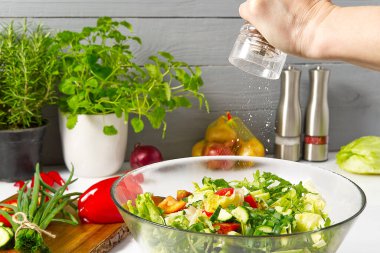 Masadaki tabakta taze sebzelerden yapılmış salata. Sebzeli ve sebzeli bir kase salata. Sebze salatası hazırlayan kadınlar. Yakın çekim. Ev mutfağı. Vejetaryen yemeği. baharatlar