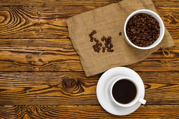 Taza de café blanco con bebida aromática de café en la mesa de madera marrón. Semillas de café en mesa de madera antigua con taza de bebida de café — Foto de Stock