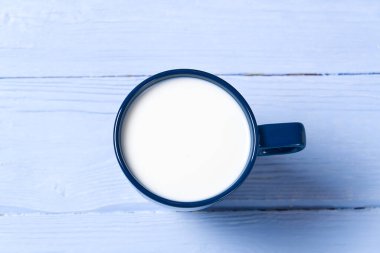 Açık mavi ahşap arka planda mavi bir bardak süt. Yukarıdan görünüm - düz yatış. Sütlü mavi kupa.