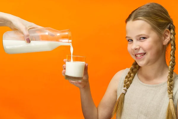 ミルクのガラスがオレンジの背景に隔離された幸せな女の子。笑顔の女の子はミルクとガラスを保持する。肖像画。牛乳をガラスに流し込み — ストック写真