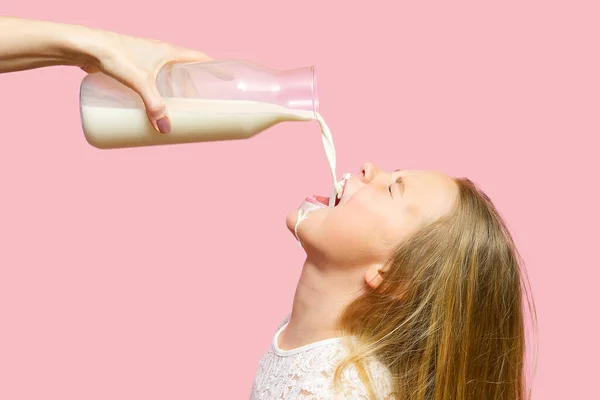 Menina feliz beber leite de garrafa Isolado no fundo rosa. Leite obtido pela boca meninas — Fotografia de Stock