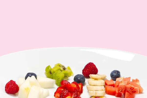 Ensalada de frutas frescas en plato blanco. Fruta mixta en plato blanco estilo comida saludable. Ensalada de frutas útiles de frutas frescas y bayas sobre fondo rosa — Foto de Stock