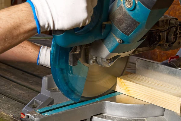 Closeup of professional cabinet makers working with electric circular saw at woodworking workshop. Skilled carpenter cutting wooden board with circular saw. Wood material production. Lumber factory