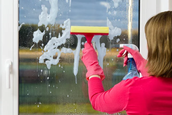 Мойка окон. Женщина в розовых резиновых перчатках моет окно в доме. Счастливая женщина в перчатках, моющая окно. Концепция услуг по уборке дома — стоковое фото