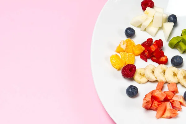 白盘上的新鲜水果沙拉.混合水果在白盘健康的食物风格。粉红色背景的新鲜水果和浆果的有益水果沙拉 — 图库照片