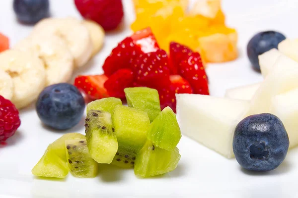 Moderne verse fruitsalade op wit bord. Gemengde vruchten in witte plaat gezond voedsel stijl. Nuttige fruitsalade van verse vruchten en bessen op witte achtergrond. — Stockfoto