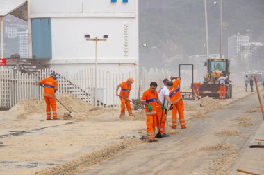 street sweepers removing sand from the leblon beach boardwalk in Rio de Janeiro, Brazil - April 5, 2020: street sweepers removing sand from the leblon beach boardwalk after a sea surf that hit the city. clipart
