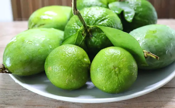 Green oranges fruit on a branch with leaves in a plate and on a tray, on wooden background