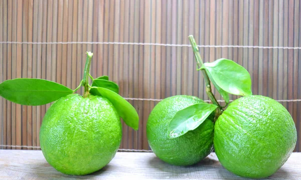 Green oranges fruit on a branch with leaves in a plate and on a tray, on wooden background