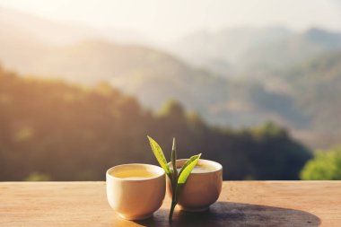 İki fincan çay yaprağı üzerinde güneş, dağlar yatay tablo ile