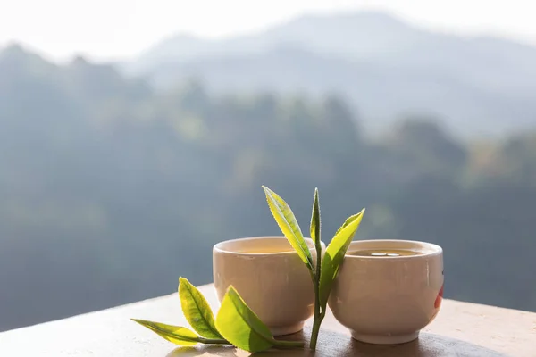 Two cup with tea leaf on table over mountains landscape with sun — Stock Photo, Image