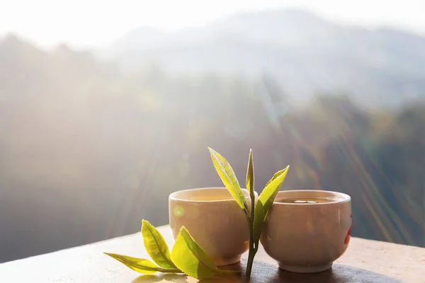 Two cup with tea leaf on table over mountains landscape with sun — Stock Photo, Image