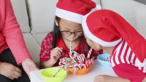圣诞节那天 孙子孙女戴着圣诞礼帽 与祖母一起玩甘蔗 — 图库视频影像