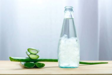 Aloe vera juice in bottle with fresh aloe vera leaves on wooden background clipart