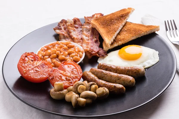 Полный английский завтрак на черной тарелке — стоковое фото