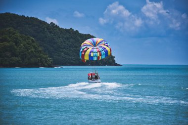 Malezya 'nın Langkawi adasındaki kumlu, egzotik ve çarpıcı Cenang sahilinin kıyısında, mavi gökyüzünün altındaki gök mavisi Andaman Denizi' nin dalgalarında paraşütle atlayan.