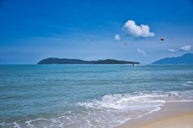 Gök mavisi gökyüzünün altındaki gök mavisi Andaman Denizi 'nin dalgalarında paraşütle atlayan Langkawi Adası' ndaki kumlu, egzotik ve çarpıcı Cenang plajının kıyılarında.,