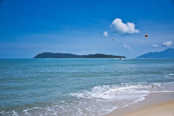 Parasailing on the waves of the azure Andaman sea under the blue sky near the shores of the arandy beautiful exotic and stunning Cenang beach in Langkawi island , — Foto de Stock