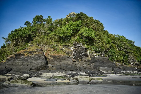 Hillside με μαύρα βράχια και πράσινα δέντρα, φυτά στις όχθες της αμμώδους όμορφη εξωτική και εκπληκτική παραλία Cenang στο νησί Langkawi — Φωτογραφία Αρχείου