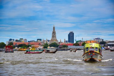 Kentin Bangkok manzarası, motorlu tekneler, uzun kuyruklu tekneler, Chao Phraya Nehri 'nde geleneksel ahşap botlar, arka planda ünlü ve inanılmaz Wat Arun Ratchavararam