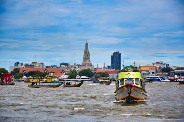 Cityscape view of Bangkok with motor boats, long tailed boats, traditional wooden boats on the Chao Phraya River with the famous and amazing Wat Arun Ratchavararam in the background