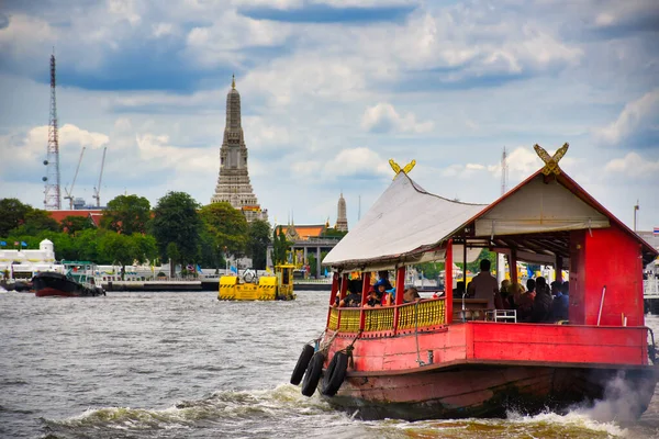 A Chao Phraya folyón egy piros fából készült hagyományos hajó halad át a híres és csodálatos Wat Arun ősi thai templomkomplexum felé. — Stock Fotó