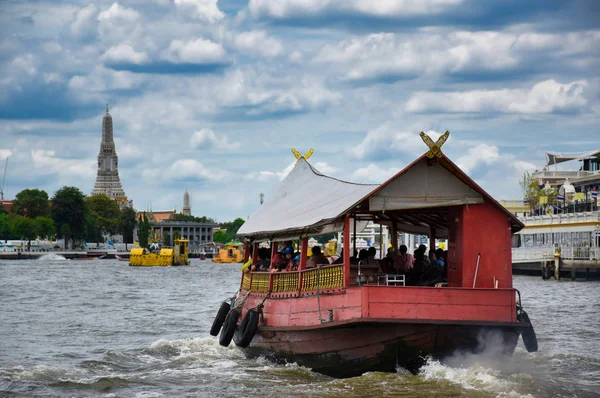 A Chao Phraya folyón egy piros fából készült hagyományos hajó halad át a híres és csodálatos Wat Arun ősi thai templomkomplexum felé. — Stock Fotó
