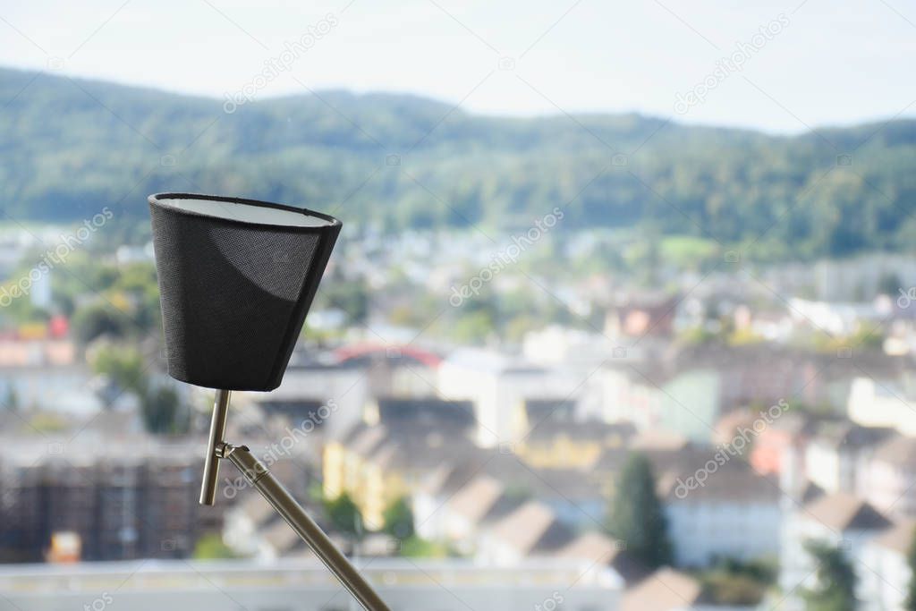 Modern flexible table lamp pointing upwards in front of a window with cityscape and mountains in the background during a sunny day