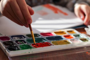 Çocuk elinde fırça ve suluboya ile çizim süreci. Çocuk akvaryumla çiziyor.