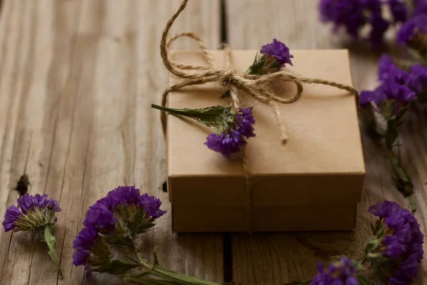 gift box with wild blue flowers on wooden background.A brown gift box with wild flower decoration on old wooden background