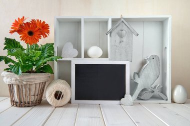 Bahar dönemi arka planında bahar süslemeleri. Farklı nesneler ve turuncu gerbera saksısı olan dolabı göster. Metnin için bir tahtaya boşluk.