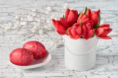 Kırmızı laleler ve beyaz arka planda iki kırmızı Paskalya yumurtası.