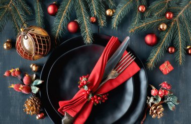 Koyu arka planda Noel menü konsepti. Yeşil ve kırmızı Noel süslemeleri ile siyah tabak ve vintage çatal. 